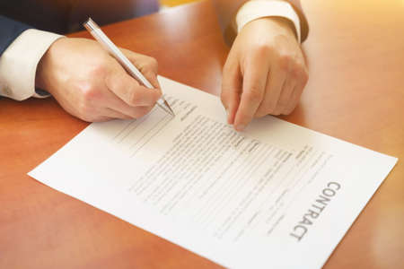 Businessman sitting at office desk signing a contract with shallow focus on signature. Business conceptの写真素材