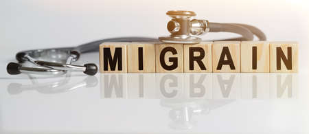 MIGRAIN the word on wooden cubes, cubes stand on a reflective white surface, on cubes - a stethoscope. Medicine conceptの写真素材