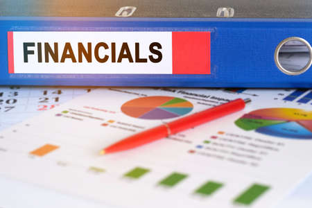 On the table are pie charts, a pen and a folder with the inscription - FINANCIALS. Business and finance concept.の写真素材
