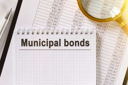 On the table are financial reports, a pen, a magnifying glass and a notebook with the inscription - Municipal bonds. Business and finance concept.の写真素材