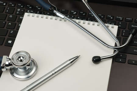 Image of a stethoscope, laptop, pen and notebook with a blank white screen, in the workplace. Space for text. Medical conceptの写真素材