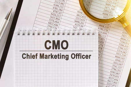 On the table are financial reports, a pen, a magnifying glass and a notebook with the inscription - CMO. Chief Marketing Officer. Business and finance concept.の写真素材