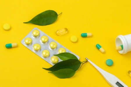 Composition of a white jar with pills, thermometer, nature green leaf on a yellow background. Medicine conceptの写真素材