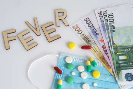 The inscription Fever, dollars, medical mask, surrounded by drugs and pills. The concept of medicine. Shot from above on a white background.の写真素材
