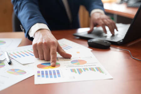 Close up Businessman hand holding pen and pointing at financial paperwork with financial network diagram. Financial conceptの写真素材