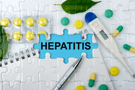 Double exposure. Puzzles with the image of tablets, a notebook, a thermometer and a pen with the inscription -HEPATITIS. The concept of medicine.の写真素材