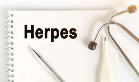 On the table are a stethoscope, a thermometer, a pen and a notebook with the inscription -Herpes. The concept of medicine.の写真素材