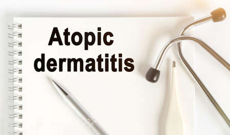 On the table are a stethoscope, a thermometer, a pen and a notebook with the inscription -Atopic dermatitis. The concept of medicine.の写真素材
