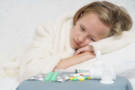 A sick teenage girl lies on the bed and looks at the medicine. Medical concept.の写真素材