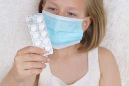 Sick teenage girl is looking through the packaging with pills. Medical concept.の写真素材