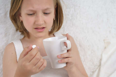 A sick teenage girl takes pills and drinks them with water. Medical concept.の写真素材