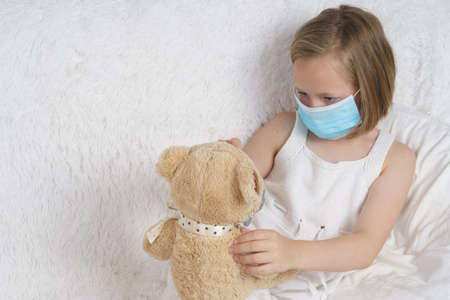 A sick teenage girl is playing with a toy wearing a protective mask. Medical concept.の写真素材