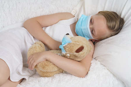 A sick teenage girl is playing with a toy wearing a protective mask. Medical concept.の写真素材