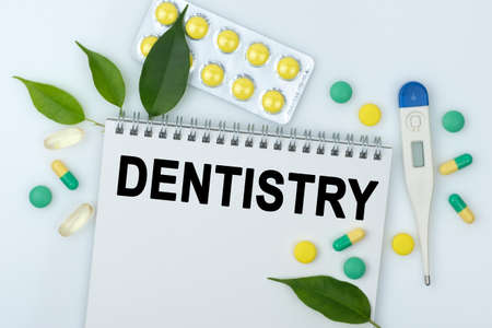 On the table are pills, a thermometer, leaves and a notebook with the inscription -DENTISTRY. The concept of medicine.の写真素材