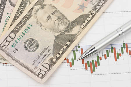US dollars and technical chart of financial instruments on a table with a metallic ballpoint pen and calculator. Forex and currency analysis concept.の写真素材
