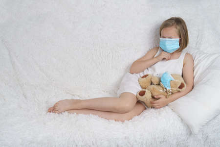 A sick teenage girl is playing with a toy wearing a protective mask. Medical concept.の写真素材