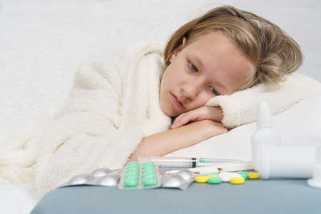A sick teenage girl lies on the bed and looks at the medicine. Medical concept.の写真素材