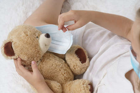 Sick teenage girl puts on a medical protective mask for a toy. Medical concept.の写真素材