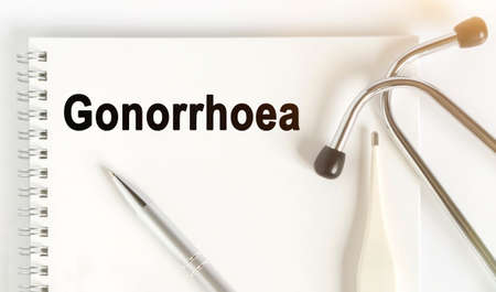 On the table are a stethoscope, a thermometer, a pen and a notebook with the inscription -Gonorrhoea. The concept of medicine.の写真素材
