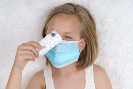 Sick teenage girl is looking through the packaging with pills. Medical concept.の写真素材