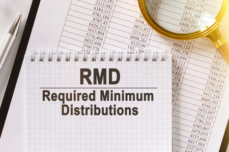 On the table are financial reports, a pen, a magnifying glass and a notebook with the inscription - RMD. Required Minimum Distributions. Business and finance concept.の写真素材