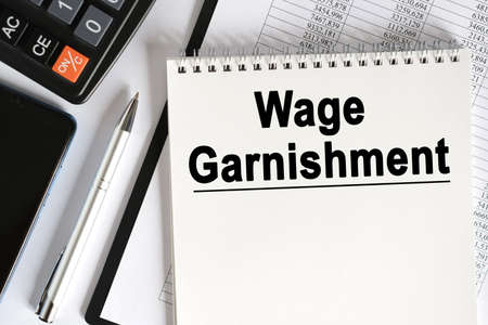 On the table lies a smartphone, a calculator and a notebook with the inscription- Wage Garnishment. Business conceptの写真素材