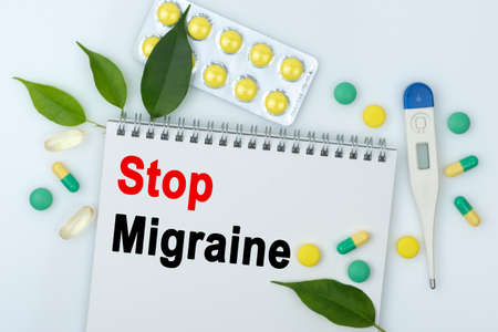 On the table are pills, a thermometer, leaves and a notebook with the inscription -Stop Migraine. The concept of medicine.の写真素材