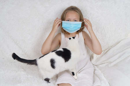 Sick teenage girl in a protective mask, next to her is a cat. Medical concept.の写真素材