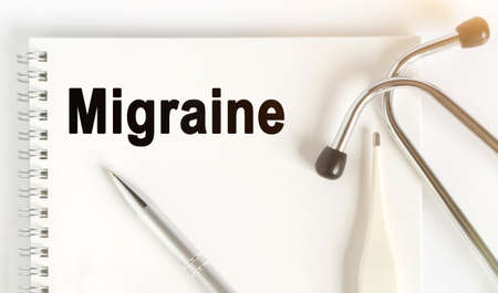 On the table are a stethoscope, a thermometer, a pen and a notebook with the inscription -Migraine. The concept of medicine.の写真素材