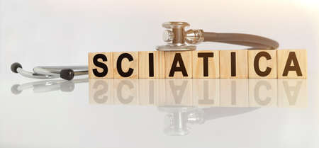 SCIATICA the word on wooden cubes, cubes stand on a reflective white surface, on cubes - a stethoscope. Medicine conceptの写真素材