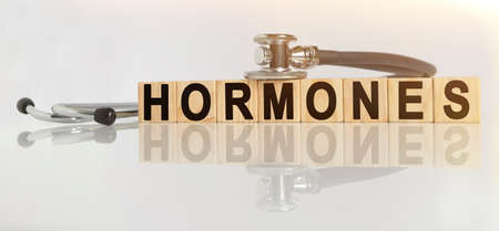 HORMONES the word on wooden cubes, cubes stand on a reflective white surface, on cubes - a stethoscope. Medicine conceptの写真素材
