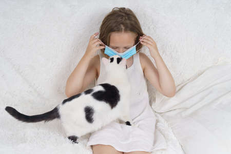 Sick teenage girl in a protective mask, next to her is a cat. Medical concept.の写真素材