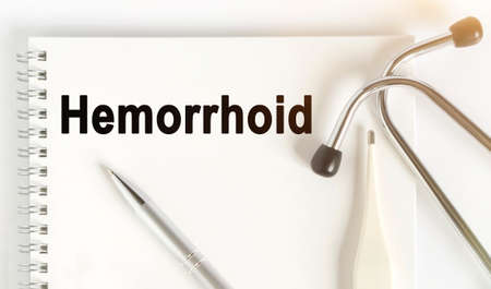 On the table are a stethoscope, a thermometer, a pen and a notebook with the inscription -Hemorrhoid. The concept of medicine.の写真素材