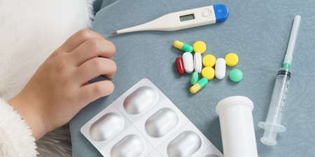 A girl takes a thermometer from the table where the medicines are. Medical concept.の写真素材