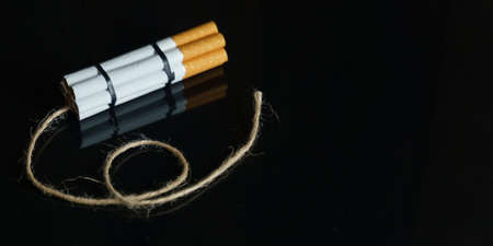 The concept of medicine is the fight against smoking. Cigarettes are twisted into a dynamite checker with a filament on a black reflective surface.の写真素材