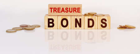 Business and economics concept. On a white reflective surface are coins and wooden cubes with the inscription - TREASURE BONDSの写真素材