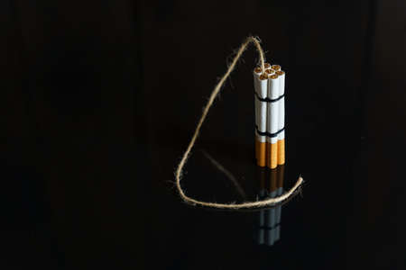 The concept of medicine is the fight against smoking. Cigarettes are twisted into a dynamite checker with a filament on a black reflective surface.の写真素材