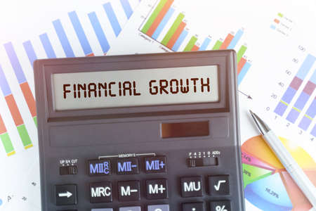The concept of business and finance. On the table are financial charts and a calculator, on the electronic board of which is written the text - FINANCIAL GROWTHの写真素材