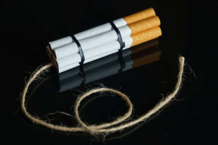 The concept of medicine is the fight against smoking. Cigarettes are twisted into a dynamite checker with a filament on a black reflective surface.の写真素材