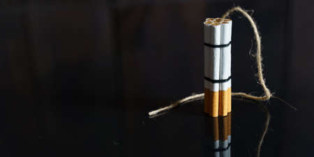 The concept of medicine is the fight against smoking. Cigarettes are twisted into a dynamite checker with a filament on a black reflective surface.の写真素材