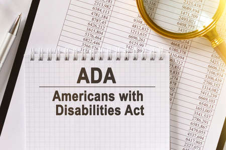 On the table are financial reports, a pen, a magnifying glass and a notebook with the inscription - ADA. Americans with Disabilities Act. Business and finance concept.の写真素材