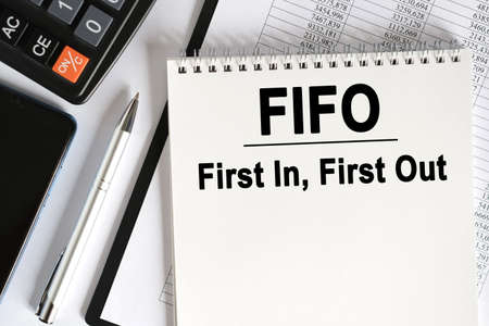 On the table lies a smartphone, a calculator and a notebook with the inscription- FIFO. First In, First Out. Business conceptの写真素材