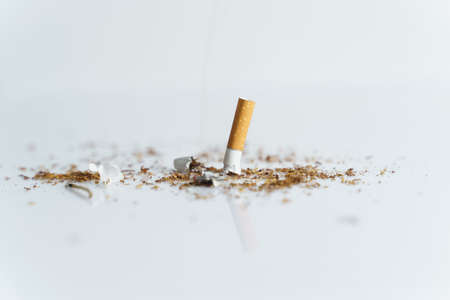 The concept of medicine is the fight against smoking. The cigarette butt is quenched among tobacco on a white reflective surface.の写真素材