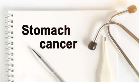 On the table are a stethoscope, a thermometer, a pen and a notebook with the inscription -Stomach cancer. The concept of medicine.の写真素材