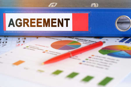 On the table are pie charts, a pen and a folder with the inscription - Agreement. Business and finance concept.の写真素材