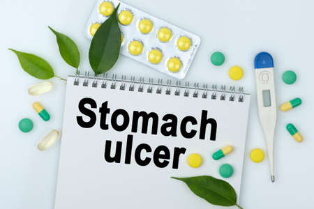 On the table are pills, a thermometer, leaves and a notebook with the inscription -Stomach ulcer. The concept of medicine.の写真素材