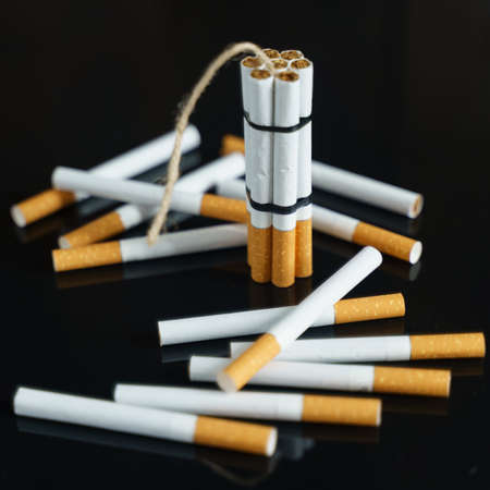 The concept of medicine is the fight against smoking. Cigarettes, in the form of checkers with dynamite, stand among the scattered cigarettes on a black reflective surface.の写真素材