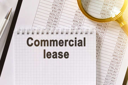 On the table are financial reports, a pen, a magnifying glass and a notebook with the inscription - Commercial lease. Business and finance concept.の写真素材