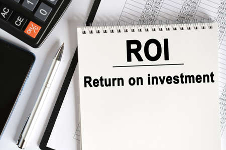 On the table lies a smartphone, a calculator and a notebook with the inscription- ROI. Return on investment. Business conceptの写真素材