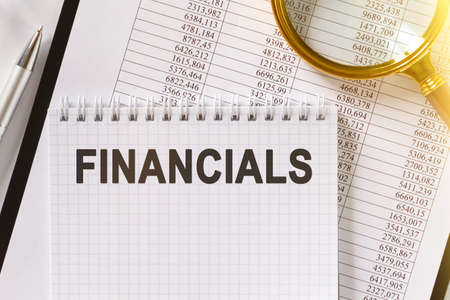 On the table are financial reports, a pen, a magnifying glass and a notebook with the inscription - FINANCIALS. Business and finance concept.の写真素材